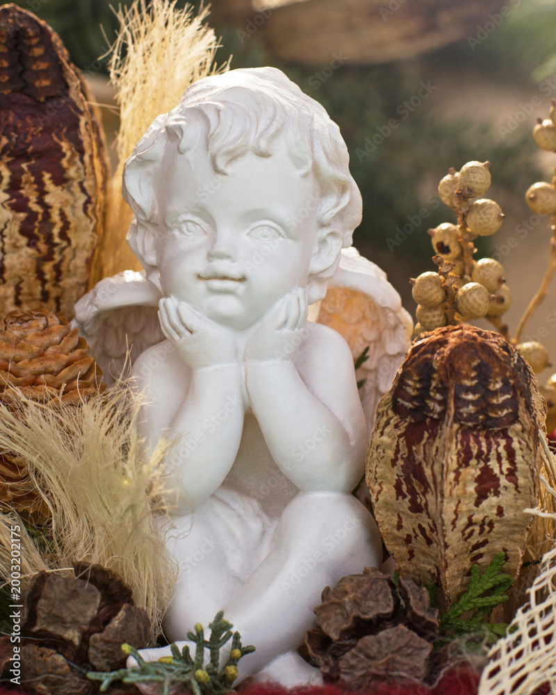 Naklejka premium Statue of a child angel surrounded by plants and natural decorations in a cozy setting