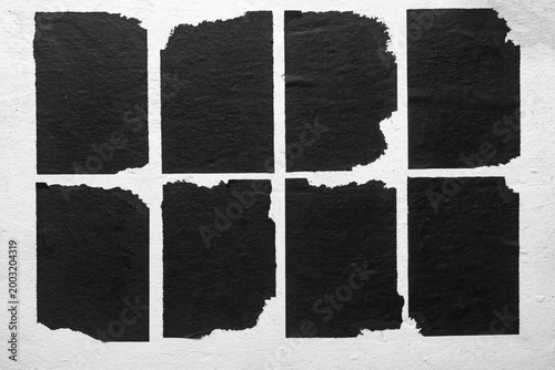 several old black torn posters on a white wall
