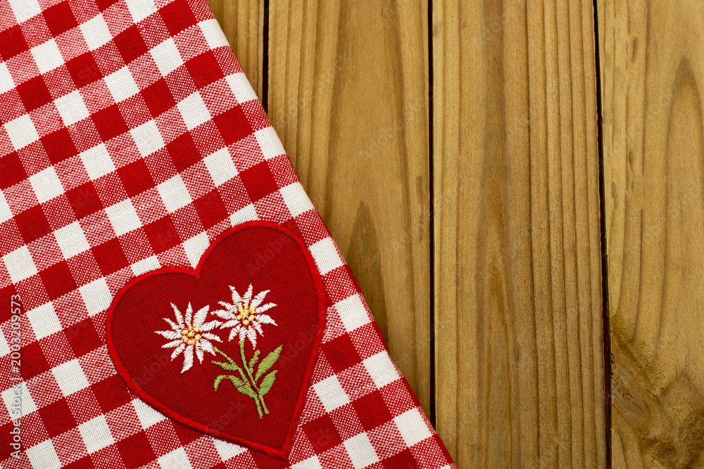 Obraz premium Checkered tablecloth with heart patch featuring flowers on wooden surface during a casual dining setting