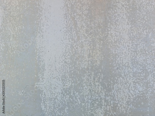 Close-up texture of peeling white paint on a light gray concrete wall. Abstract background with subtle cracks and weathered surface. Ideal for minimalist design and wallpaper.