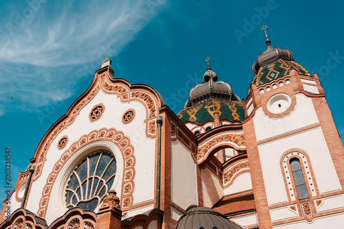 Decorative facade of Subotica Synagogue under vivid blue sky in Subotica, Serbia. Art Nouveau architecture with ornate brickwork and ceramic roof details.