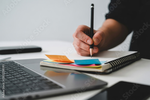 Student taking notes in notebook next to laptop, pen writing in book
