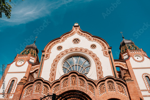 Decorative facade of Subotica Synagogue under vivid blue sky in Subotica, Serbia. Art Nouveau architecture with ornate brickwork and ceramic roof details.