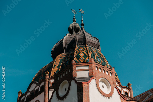 Ornate dome and tiled roof of Subotica Synagogue against blue sky in Subotica, Serbia. Decorative Art Nouveau architecture with rich historic detail.
