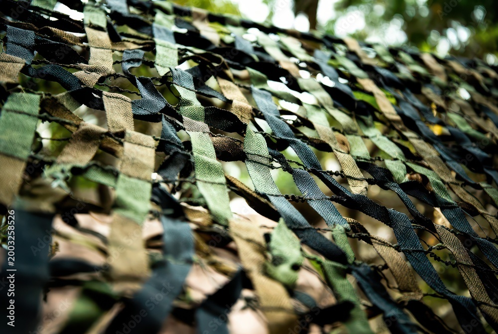 Fototapeta premium Close-up abstract view of a camouflage net with blurred green foliage in the background