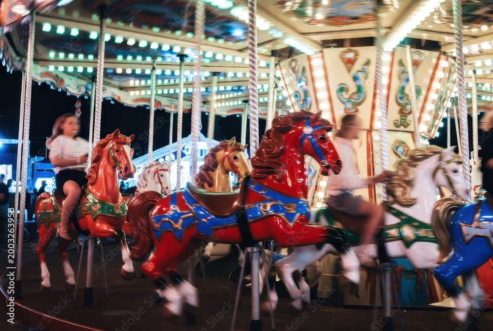 Fototapeta premium Motion blur captures the joy of children riding a brightly lit carousel at night