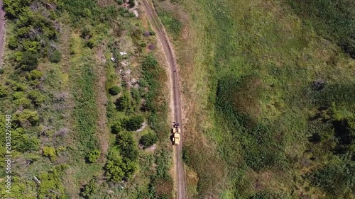 Aerial view of tractor with a cable drum laying fiber optic hawser at countryside. Workers guiding and adjusting rope to ensure proper placement under ground for communication or power infrastructure