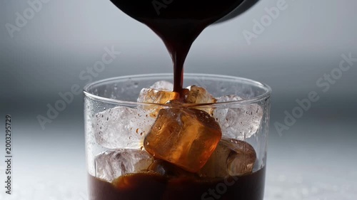 Iced coffee with ice cubes and coffee pour close up