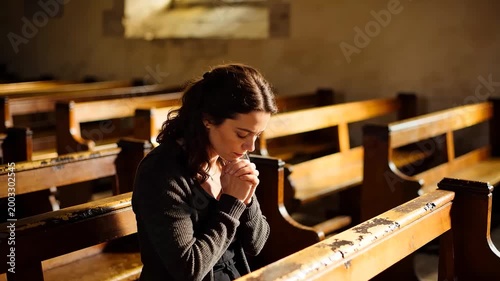Young adult woman praying with clasped hands in a sunlit church pew, spiritual contemplation and faith in a traditional chapel setting for peace and reflection