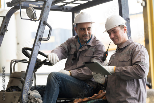 Engineers in safety gear discussing work using tablet at work. Male worker wearing safety uniform, helmet and gloves at work. Unity and teamwork concept