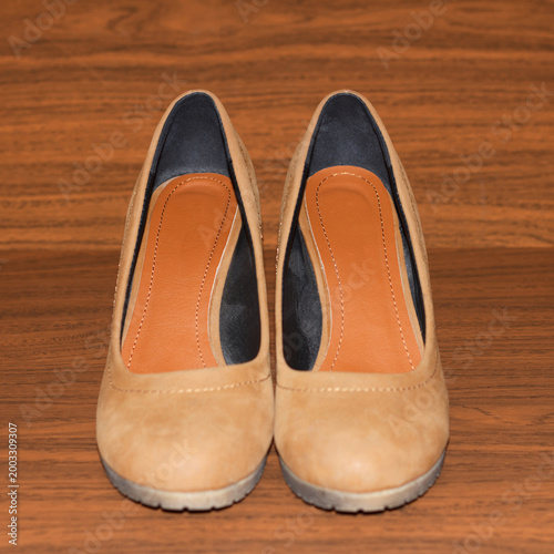 Fotografia A pair of stylish women's tan wedge heel shoes sit on a dark wood grain surface