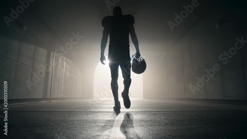 Silhouette of an American football player walking through a dark tunnel toward a bright stadium light, professional athlete preparing for competition and victory