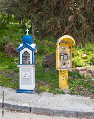 An unmolested Kandylakia or roadside shrine next to a defaced and vandalised public phone, Nafplio, Greece