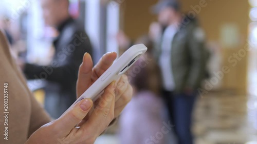 Close-up of hand holding smartphone. Background blurred with people walking. Urban setting with natural lighting. Focus remains on phone interaction