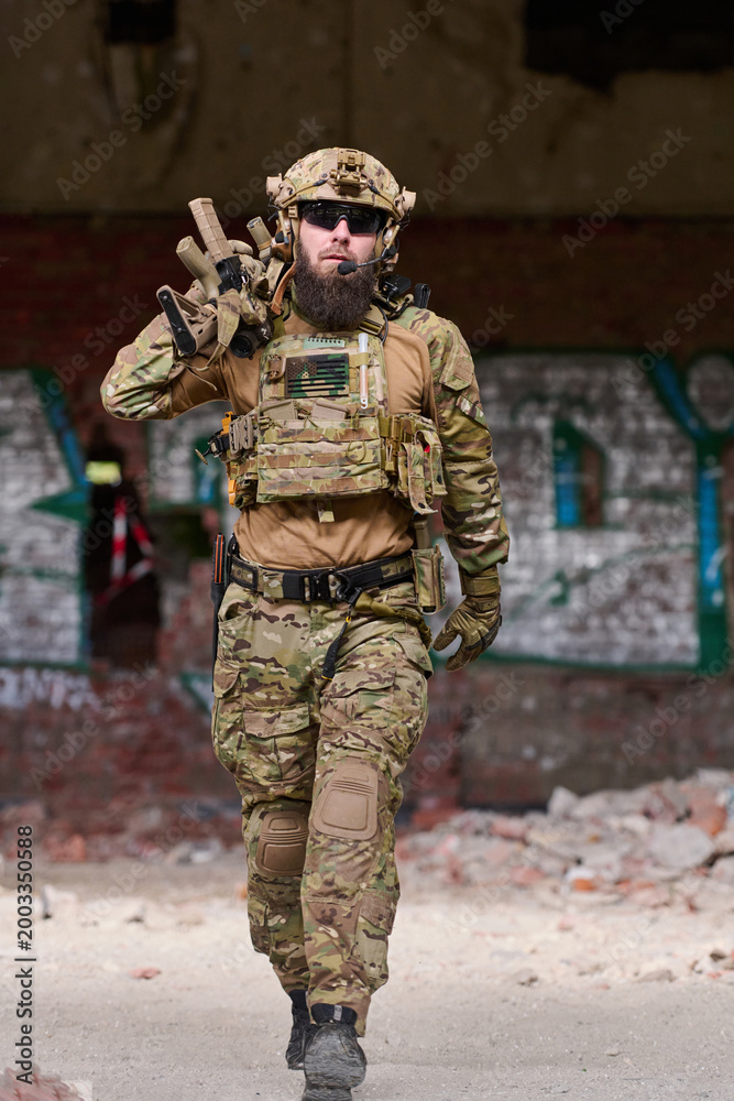 Fototapeta premium Armed Tactical Soldier in Camouflage Gear Walking Through Urban Ruins With Rifle and Helmet