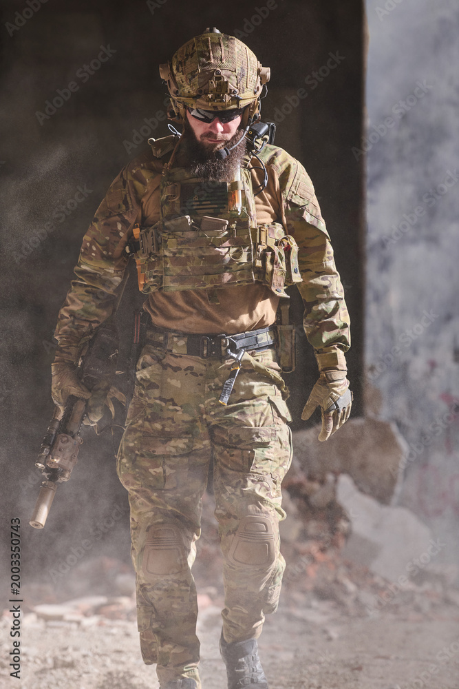 Fototapeta premium Soldier in Tactical Gear Walking Through Dusty Urban Ruins With Rifle and Camouflage Uniform