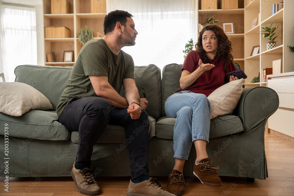 Φωτογραφία Jealous man confronting woman about mobile phone conversation at home