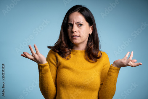 Tableau sur toile Puzzled young female shrugging shoulders isolated against blue studio backdrop