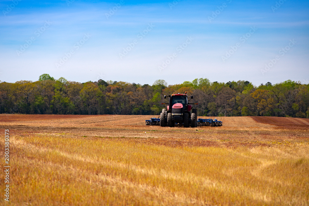 Fototapeta premium Agriculture fieldwork. Agricultural field landscape. Farm field with tractor. Farmland machinery. Plowed field tractor. Tilled field equipment. Rural farm scene.
