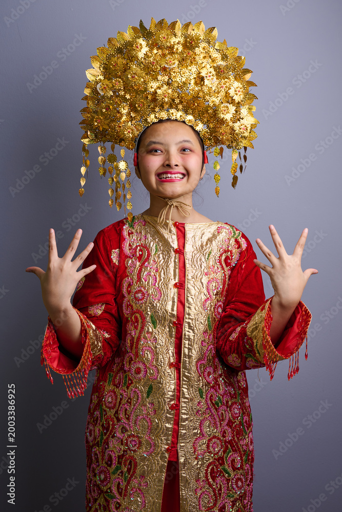 Obraz premium Smiling Indonesian Asian Girl in Red and Gold Traditional Ceremonial Costume With Ornate Golden Headdress