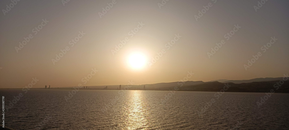 Fototapeta premium Sunrise over mountains, sea, and city with a glowing orange sky.