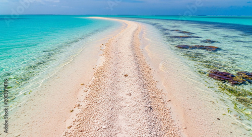 Pristine tropical sandbar extends into crystal clear turquoise ocean, with vibrant coral reefs under a bright blue sky, an idyllic island paradise