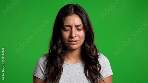 Crying Woman in Studio: A young woman stands against a green studio background, her face etched with profound sadness as tears stream down her cheeks.