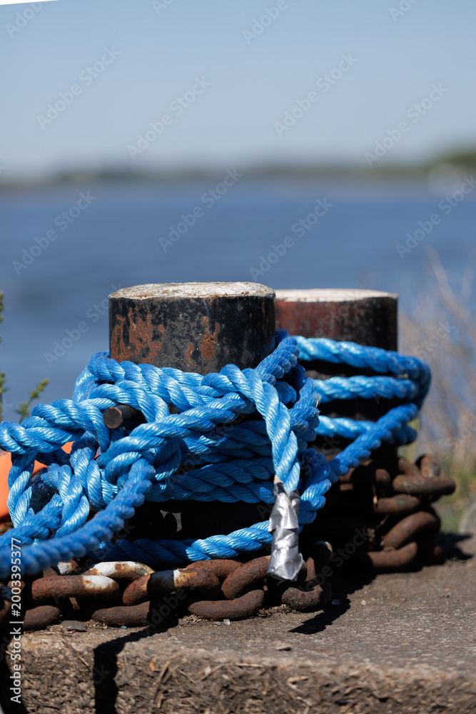 Fototapeta premium Relaxing Seaside Setting Emphasizing Rusted Post Entwined With Twisted Blue Cord And Radiant Sunlight