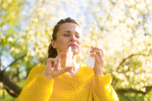 Foto A woman with closed eyes prepares to use her nasal spray, managing hay fever symptoms amidst the golden light and blooming trees of a spring orchard