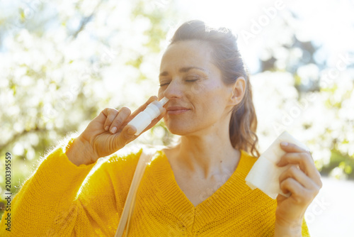 Photos A woman finds relief from spring pollen allergies by using a nasal spray bottle, eyes closed in a calm moment among blooming garden trees
