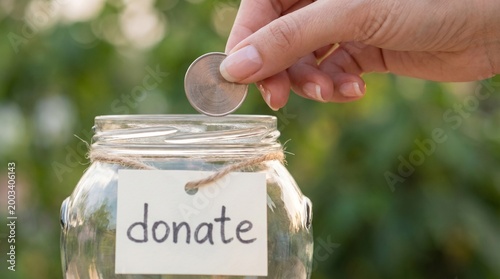 Coin of Kindness: A tender moment captured as a hand carefully places a coin into a transparent jar, symbolizing the spirit of donation and heartfelt giving.