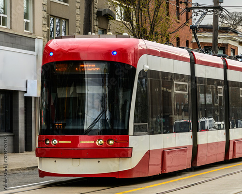 Quadro su tela Toronto streetcar travelling on Queen Street East with headlights illuminated on a spring morning, urban storefronts visible in background