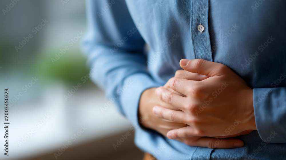 Fototapeta premium Close-up of a man's hands clutching his stomach conveying a sense of discomfort or pain possibly related to digestive problems. Defocused background. Hands clutch stomach,