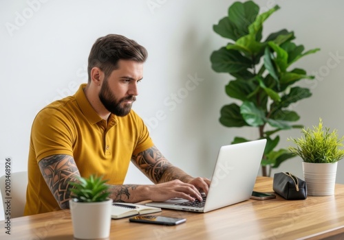 Man with tattoos working on a laptop at a desk in a bright office