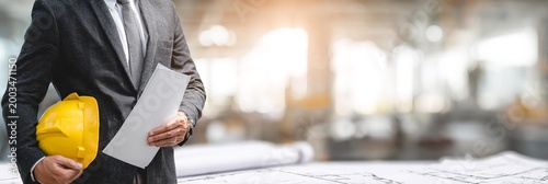 An engineer is standing in front of building site with papers.