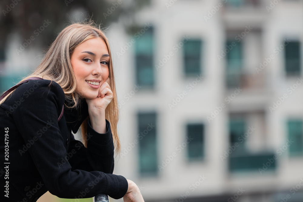 Fototapeta premium beautiful young woman leaning against the street looking at the camera, smiling, with copy space