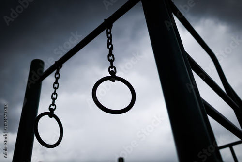 metal exercise rings hang from a frame against a dark sky filled with clouds before a storm in a park