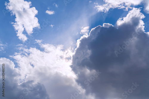 Blue sky with large cumulus clouds and sun rays shining through gaps. Nature sky photography. Weather and climate concept. Design for wallpaper, banner, poster, background, header. Low angle view with