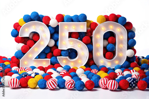 Large illuminated number 250 surrounded by colorful red, white, and blue decorative balls on a white background, symbolizing US Independence Day celebrations and festivities