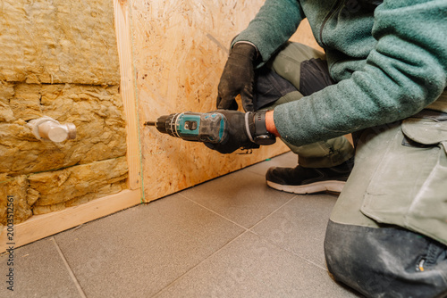 Canvas Print Male construction worker using a power drill to install wooden panels on a wall