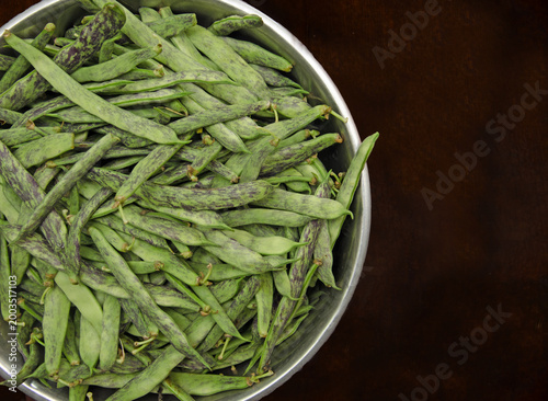 Fresh green string beans with purple stripes in a metal bowl. Raw string beans in a bowl on a dark background, top view. Organic flat string beans in a stainless steel bowl on a dark background. Raw 