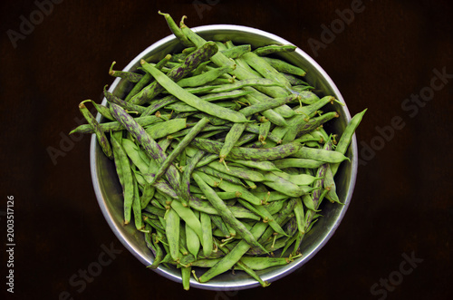 Fresh green string beans with purple stripes in a metal bowl. Raw string beans in a bowl on a dark background, top view. Organic flat string beans in a stainless steel bowl on a dark background. Raw 