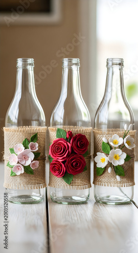 Three decorative glass bottles wrapped in burlap and adorned with handmade clay flowers.