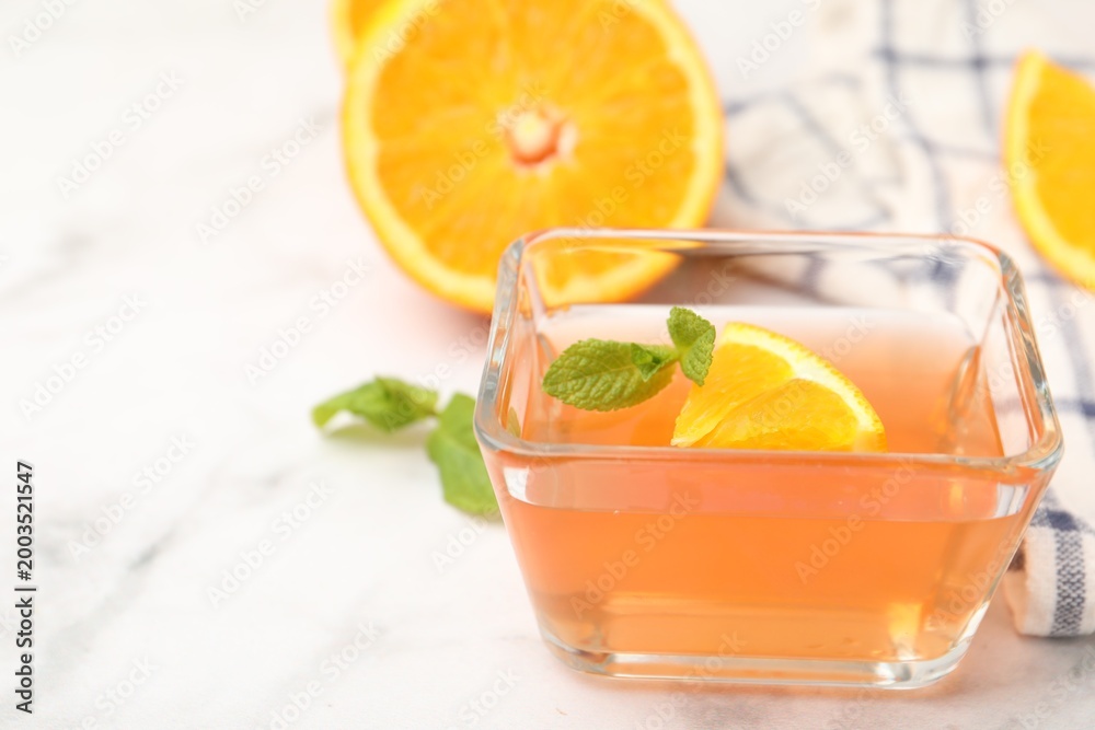 Fototapeta premium Yummy jelly in glass bowl, oranges and mint on white marble table, closeup. Space for text