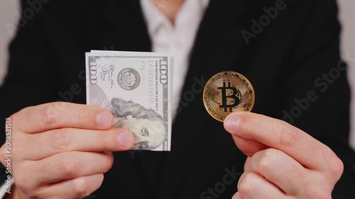 Une personne tenant un billet en dollar et un bitcoin dans ses mains, symbolisant les devises numériques et papiers. 