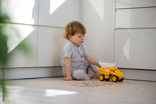 Foto Little cute child boy gather buckwheat sweeping floor with his hands at home with light interior