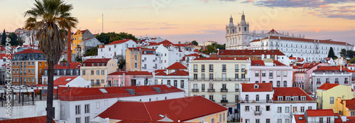 Lisbon, Portugal. Panorama of the city during sunset evening. Houses red roofs of historic old town in district Alfama in Lisboa. Palm tree in front.