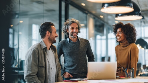 Diverse team of professionals collaborating and smiling in a modern office setting with a laptop and natural light