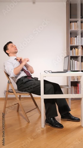 Vertical video businessman leaning back in his chair, tiredly taking off glasses, experiencing eye strain and stress from prolonged laptop use at his home office desk