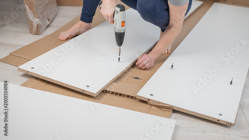 A Caucasian woman uses a screwdriver to tighten a screw while assembling a cabinet.